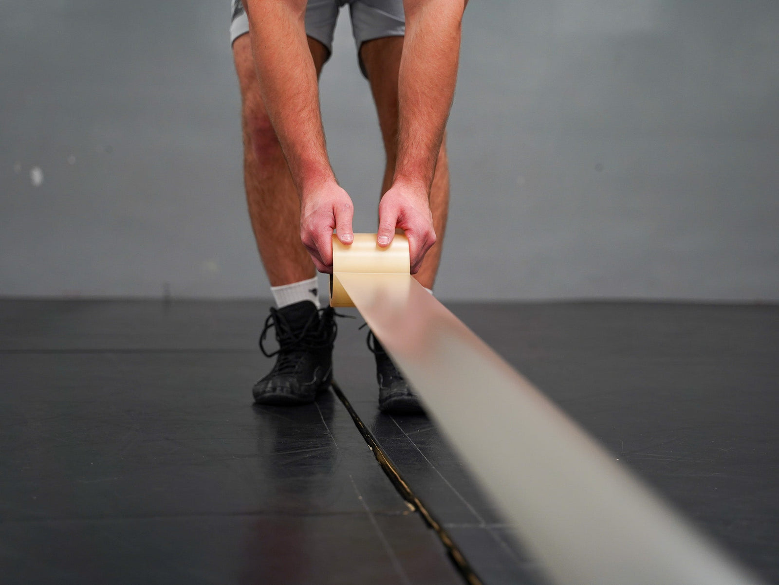 Hands applying wrestling mat tape across seam for secure fit