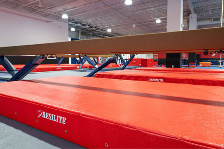 Resilite competition landing mat positioned under a balance beam for gymnastics training and competition